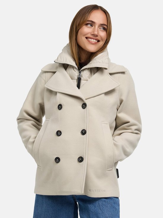 Une femme porte une courte veste beige Marikoo à double boutonnage avec un col à capuche intégré. Elle sourit, les mains dans les poches.