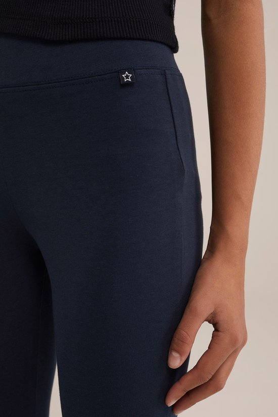 Detail van een donkerblauwe legging met een klein wit sterlogo op de linkerheup.