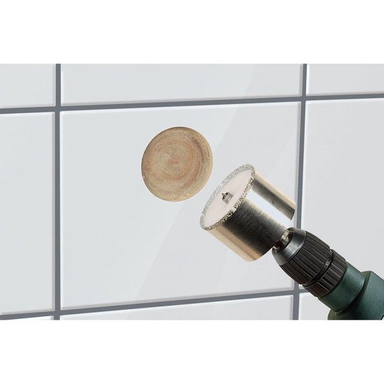 Zilverkleurige diamantboor met witte binnenkant, die een rond gat in een witte tegel maakt.