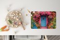 Set de table imprimé d'une maison rose, d'une porte bleue et de fleurs, à côté d'une planche à découper avec des légumes.