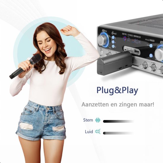 Vrolijke vrouw met witte top en spijkerbroek zingt in microfoon bij versterker.