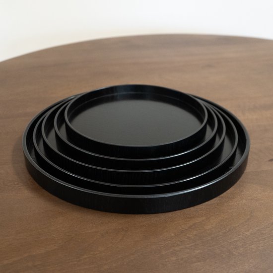 Een set van vijf zwarte, ronde dienbladen, in elkaar gestapeld op een houten tafel.