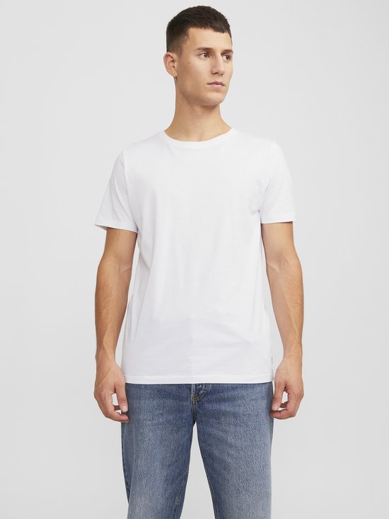 Man draagt een wit T-shirt en een spijkerbroek, kijkend weg.