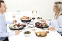 Man en vrouw zitten aan tafel, met twee Princess gourmetstellen en eten erop.