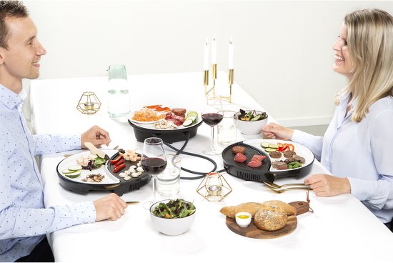 Man en vrouw zitten aan tafel, met twee Princess gourmetstellen en eten erop.