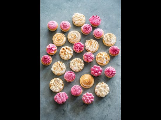 Grote selectie van roze en witte gebakjes, waaronder cupcakes en meringue koekjes.