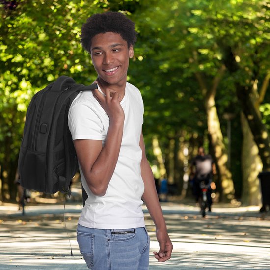 Jonge man met rugzak op zijn schouder, wandelend in een park met bomen.