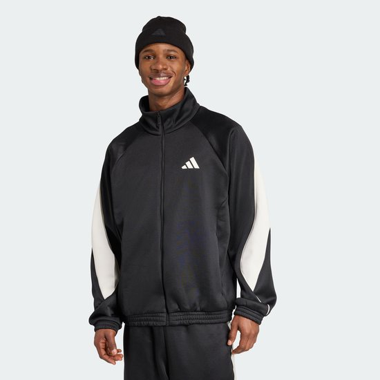 Man met zwarte jas met beige mouwen en een zwarte muts. Jas heeft een wit adidas logo op de borst.