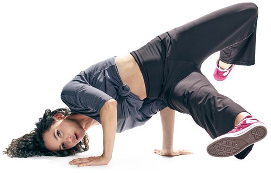 Vrouw in donkergrijze top en broek, dansend op de grond, met roze sneakers.