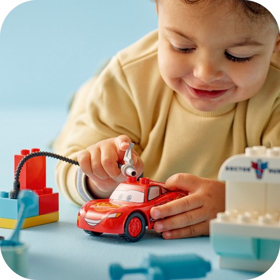 Jongetje speelt met rode LEGO Duplo Lightning McQueen auto en de doktersgarage. Sluit de slang aan op de auto.