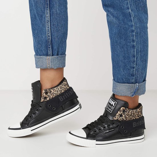 Voeten van een persoon in blauwe jeans en zwarte hoge sneakers met panterprint details.