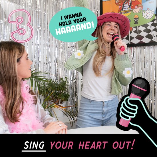 Een vrouw met een roze hoed zingt in een roze microfoon. Een andere vrouw kijkt toe. Tekst in een ballon: 'I wanna hold your HAAAND!'