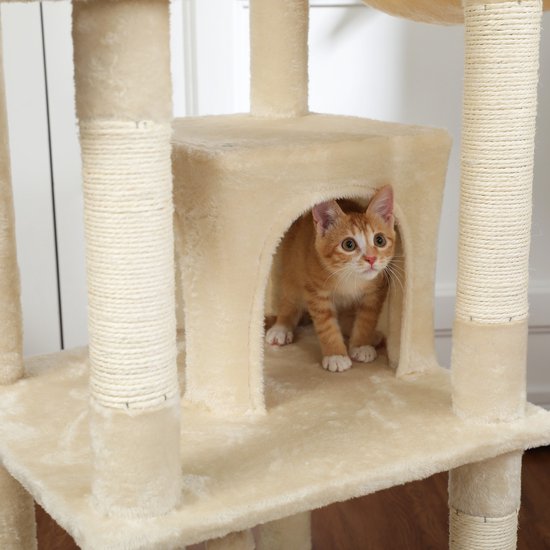 Een oranje gestreepte kitten kijkt uit een deuropening in een crèmekleurige kattenboom.