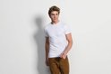 Man in wit t-shirt en bruine broek, witte achtergrond.