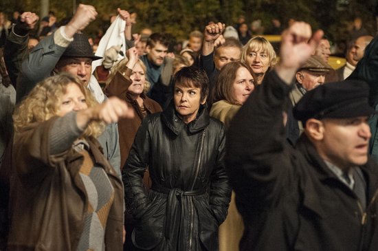 Een groep mensen met gebalde vuisten op een demonstratie. Een vrouw in het midden draagt een zwarte leren jas.