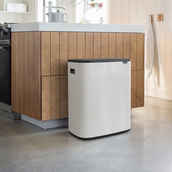 Vrouw met witte jurk opent de witte Brabantia Bo Touch Bin prullenbak in een lichte keuken.