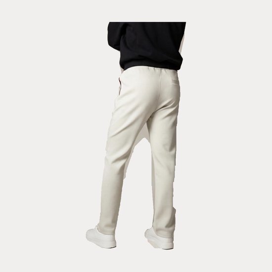 Achterkant van beige sportbroek met rode accenten gedragen door een model met zwarte trui en witte sneakers.