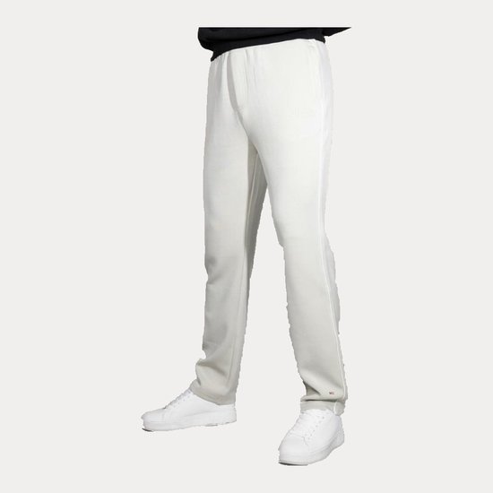 Model draagt een beige sportbroek met witte bies en rode details, gecombineerd met een zwarte trui en witte sneakers.