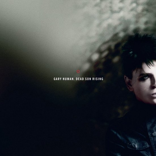 Gary Numan avec cheveux foncés et maquillage, pochette d'album Dead Son Rising sur fond sombre et granuleux.