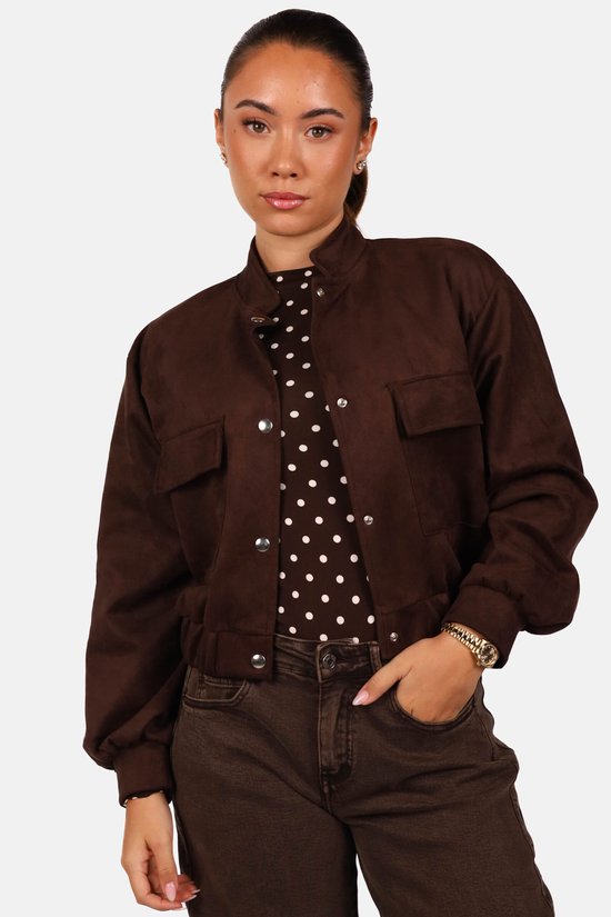 Model draagt een bruin suède-look bomberjack met drukknoopsluiting over een top met stippen.