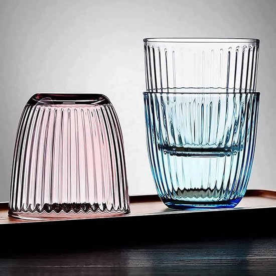 Un verre rose à l'envers à côté de deux verres bleus empilés remplis d'eau.