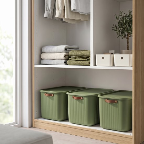 Drie groene opbergboxen met leren handgrepen staan onder gestreepte vouwbare kleding in een kast.