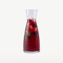 Glazen karaf gevuld met rood fruit, ijs en munt.