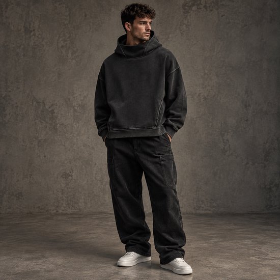 Man in zwarte, oversized hoodie met hoge hals en bijpassende zwarte cargo-broek.