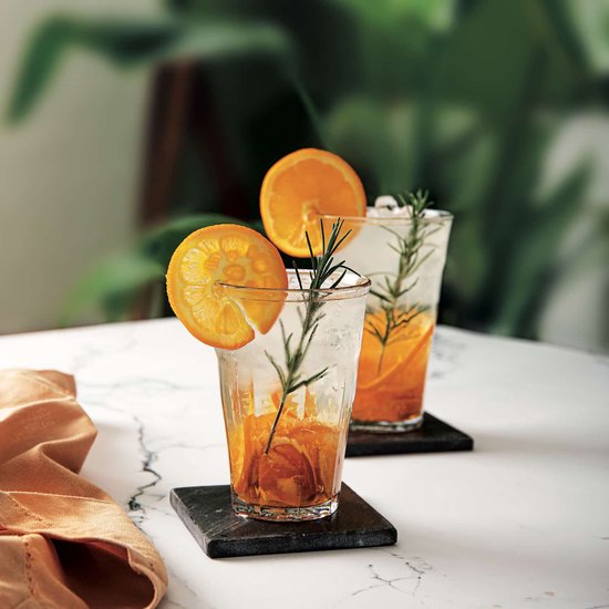 Deux verres Duralex Picardie transparents avec cannelures verticales, remplis d'eau glacée et de rondelles d'orange avec du romarin.