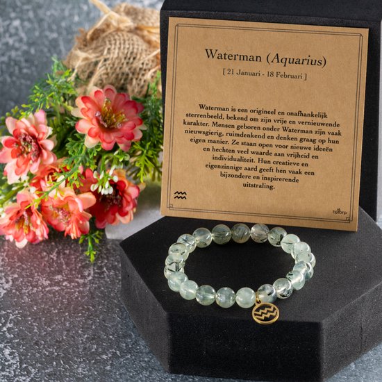 Prehniet edelsteen armband met gouden Waterman bedel, naast een kaart over Waterman en een boeket bloemen.