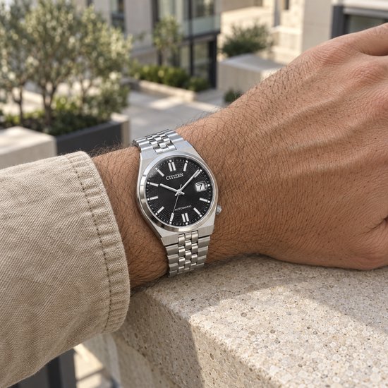 Een zilverkleurig horloge met een zwarte wijzerplaat gedragen op een mannenpols.