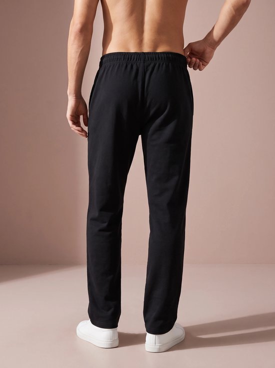 Homme vu de dos portant un pantalon de sport noir et des baskets blanches.