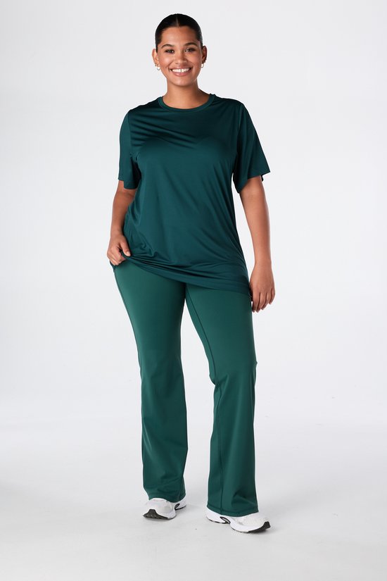 Model in donkergroen sportshirt met relaxed fit en lange pasvorm, gecombineerd met een bijpassende sportbroek.