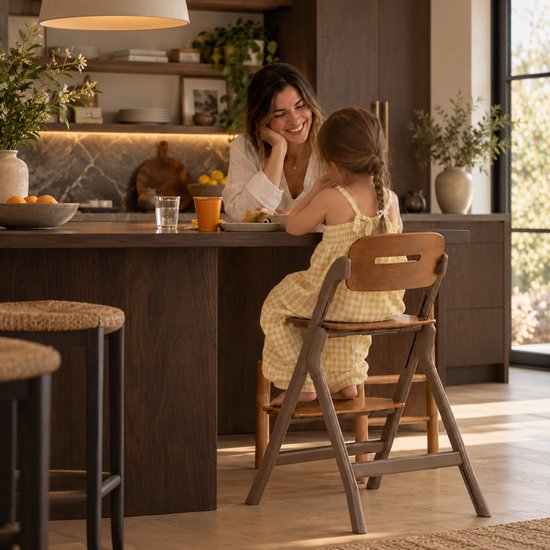 Kind in geel ruitjespak zittend op een donkerbruine Deryan kinderstoel tegenover een lachende vrouw aan tafel.