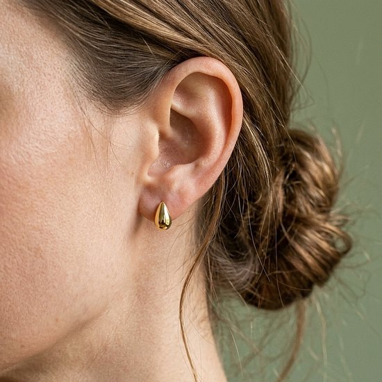 Goudkleurige druppelvormige oorknopjes gedragen door een vrouw met haar haar in een knot.