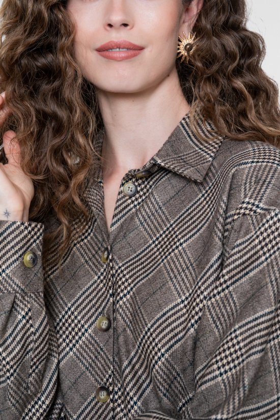 Close-up van bruine jas met ruitpatroon en knoopsluiting, gedragen door vrouw met krullend haar en oorbellen.