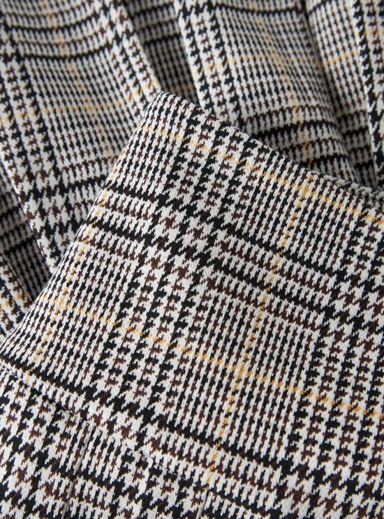 Close-up van een geplooide stof met een gedetailleerd grijs, zwart en beige ruitpatroon.
