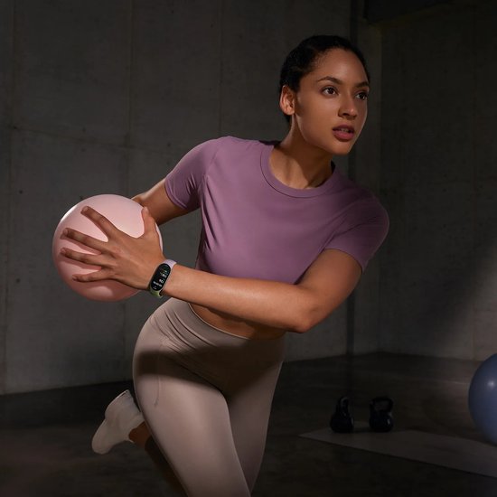 Femme en t-shirt de sport violet et legging beige s'entraînant avec un ballon, portant un tracker d'activité au poignet.