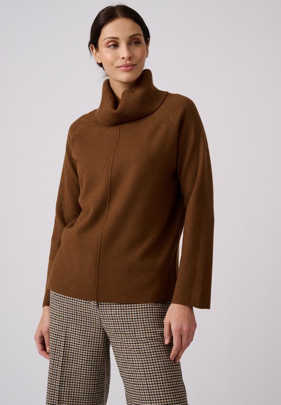 Model met een bruine coltrui met raglanmouwen en een geruite broek.