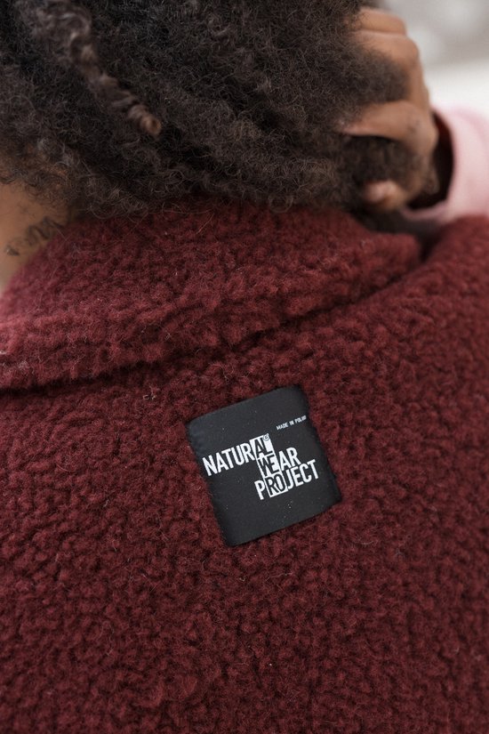 Detail van een bordeauxrood wollen label met de tekst 'Natural Wear Project' op een bodywarmer.