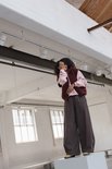 Model lacht op een wit blok in een bordeauxrode wollen bodywarmer en roze trui.