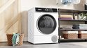 Bosch Serie 6 warmtepompdroger in een wasruimte met rekken vol handdoeken en een wasmand.