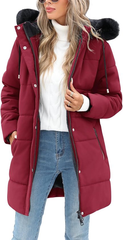 Een model draagt een dieprode gewatteerde winterjas met capuchon en zwarte bontrand, met een witte coltrui en spijkerbroek.