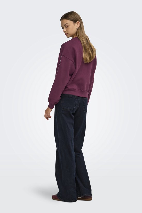 Model van achteren gezien in een paarse sweater met wijde donkerblauwe jeans.