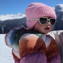 Baby in de sneeuw met roze muts en lichtgrijze hartvormige zonnebril.