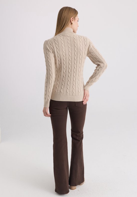Model staat in profiel van achteren, met een beige kabelgebreide trui en bruine broek.