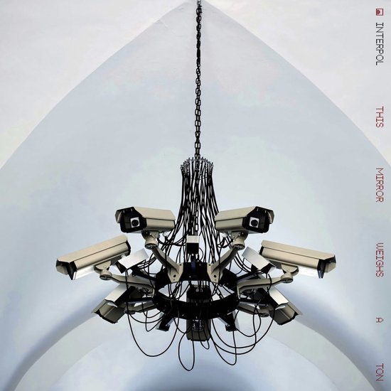 Kroonluchter gemaakt van bewakingscamera's tegen een boogvormige witte achtergrond met de tekst 'This Mirror Weighs A Ton'.