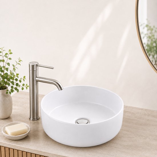 Witte opbouwwaskom met metalen afvoerplug op een beige aanrechtblad in een lichte ruimte.