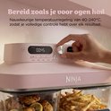 Roze Ninja airfryer met glazen schalen, digitaal bedieningspaneel bovenaan en hand die de instelknop aanpast.