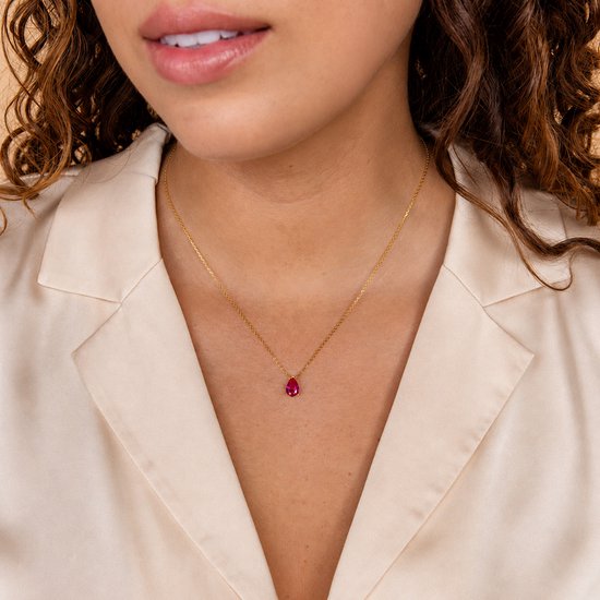 Gouden ketting met een rode robijnkleurige druppelvormige edelsteen op een vrouw met krullend bruin haar.